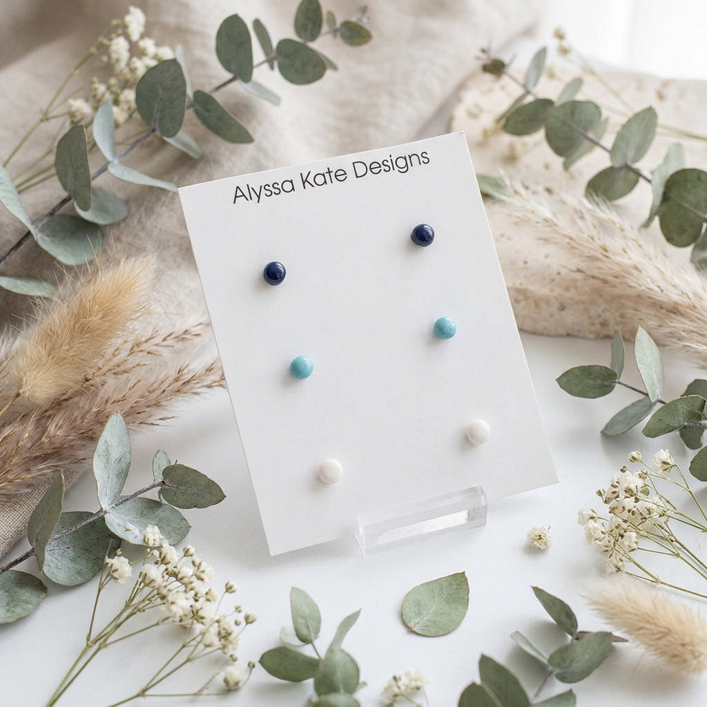Six small round stud earrings in navy, light blue, and white.