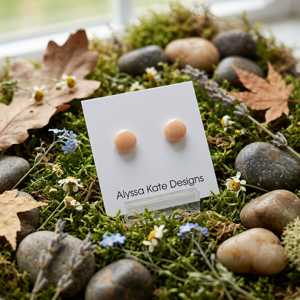 A pair of small round stud earrings in a light peach-beige color.