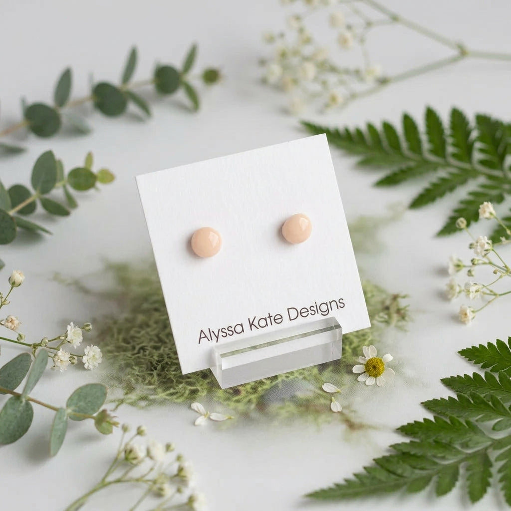 A pair of small round stud earrings in a pale peach-beige color.
