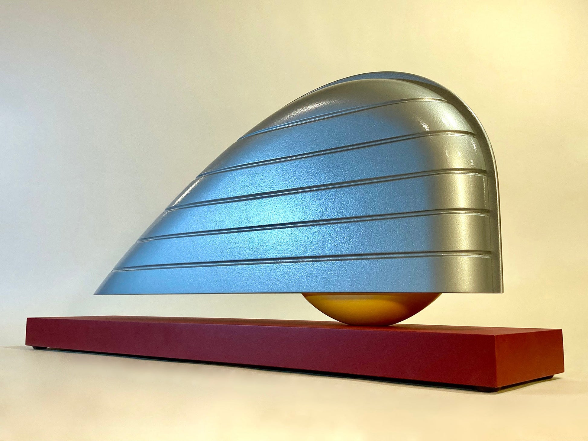 Silver shape with grooves with a yellow crescent under it resting atop a red plank of wood. 15"x34"x7" painted wood Sean O'Meallie