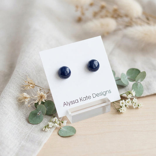 A pair of small round dark blue stud earrings.