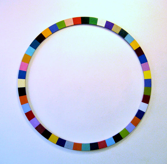 A wooden sculpture in the shape of a circle. The circle is made up of many small squares that are different colors including blue, green, pink, yellow, and brown. 2010 60”x60”x.75” painted wood by Sean O'Meallie