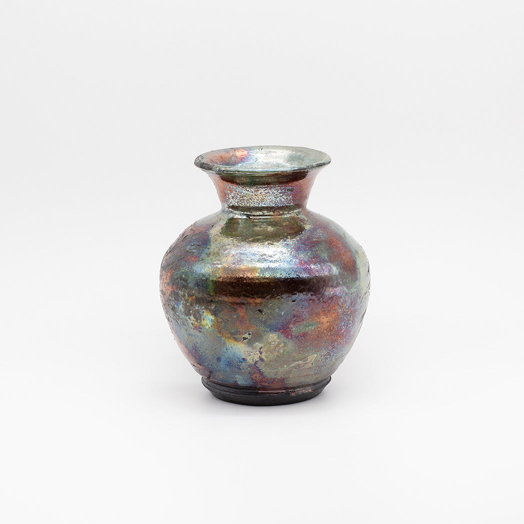 A small ceramic vase with a rounded body, flared rim, and dark base, covered in an iridescent metallic glaze showing purple, blue, green, and copper tones.