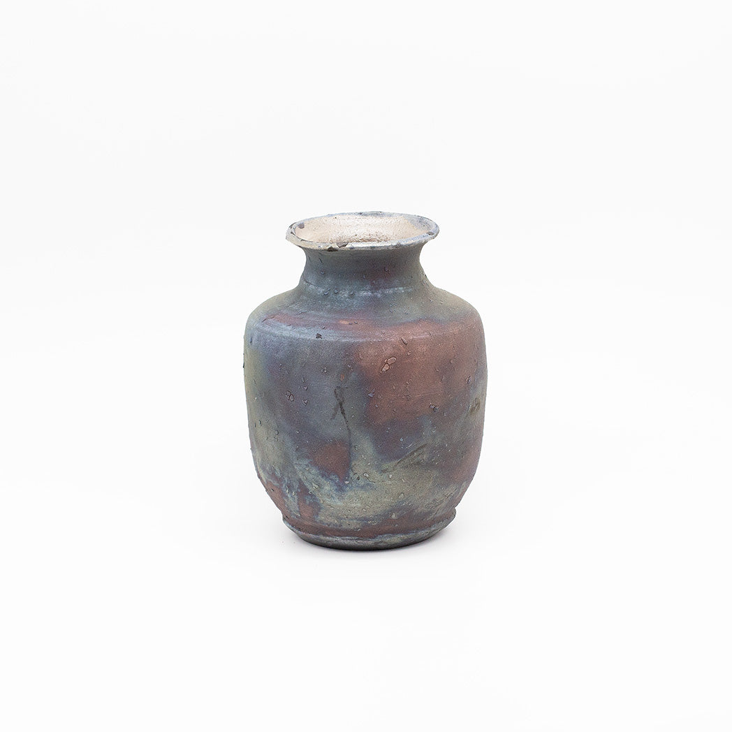 A small handmade ceramic vase with a rounded body, narrow flared neck, and slightly uneven rim, featuring a mottled glaze of blue, purple, brown, and beige tones.