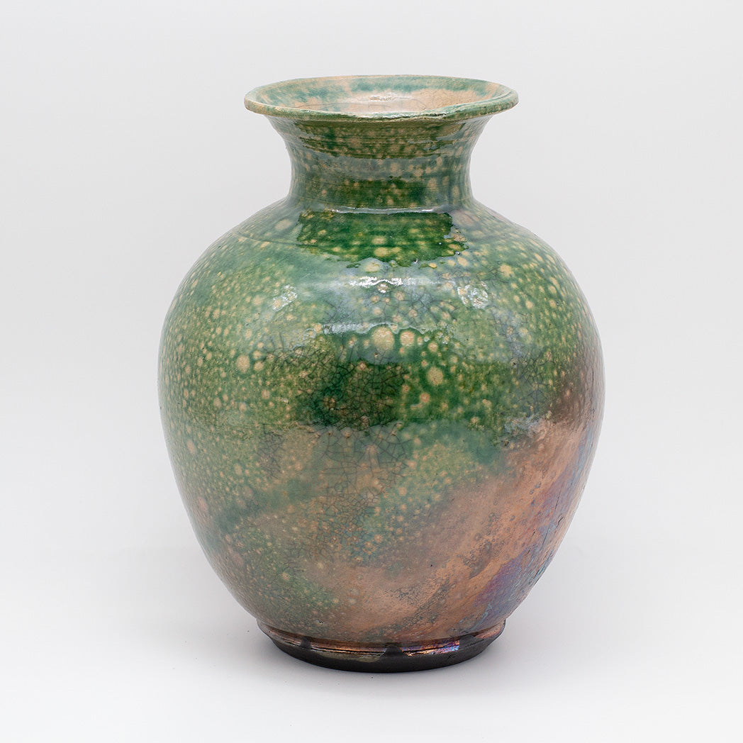 A ceramic vase with a rounded body, short flared neck, and small footed base, featuring a glossy green glaze with mottled lighter green speckles and a warm brown iridescent area near the lower right side.