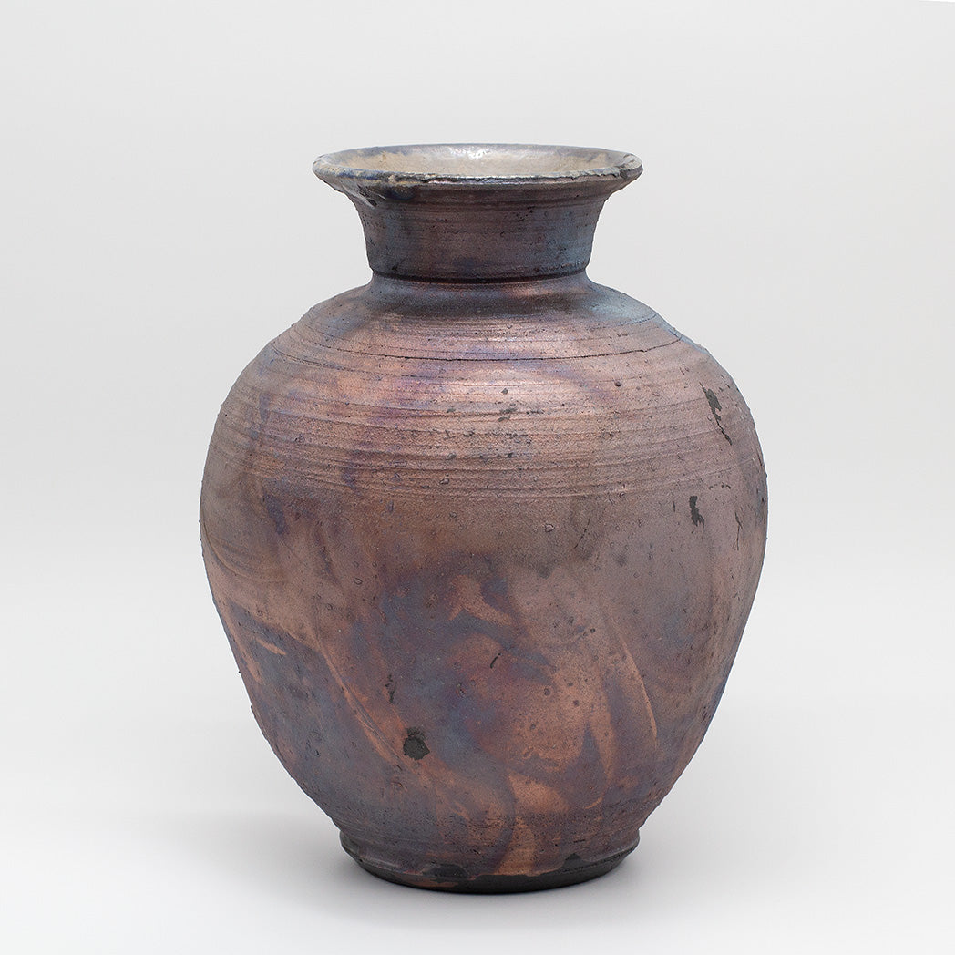 A handmade ceramic vase with a rounded body, short flared neck, and rustic textured glaze in earthy brown, bronze, and purple tones.