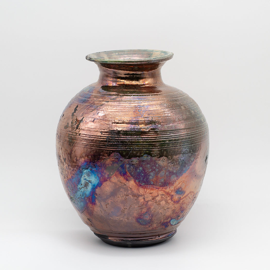 A round ceramic vase with a flared neck, featuring a metallic copper-brown glaze with iridescent blue, purple, and green shifts.