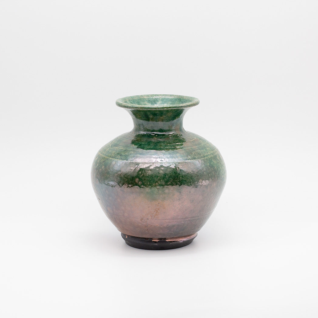 A small ceramic vase with a rounded body, flared rim, and dark base, featuring a glossy glaze that transitions from green at the top to a warm coppery-brown at the bottom.