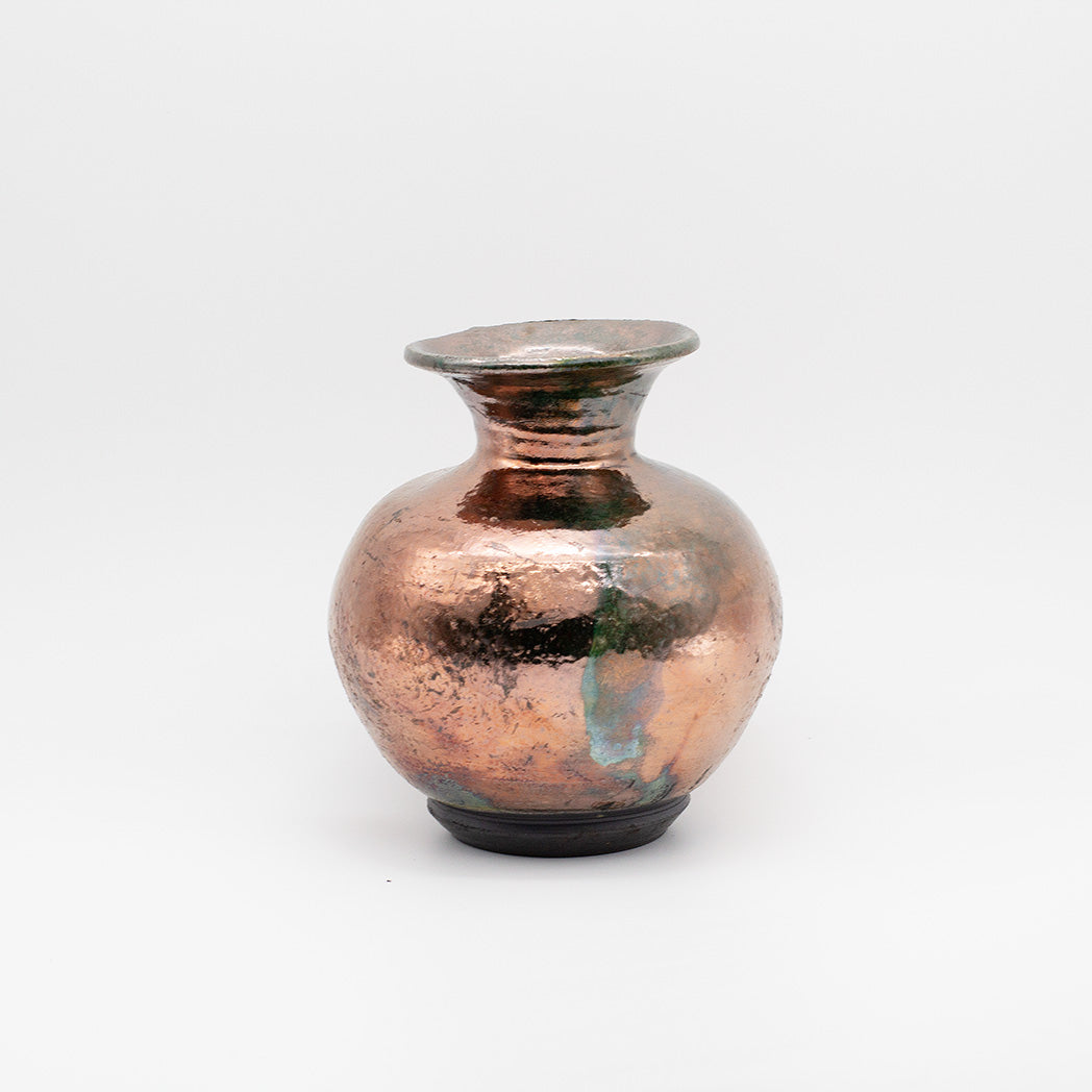 A small handmade ceramic vase with a rounded bulbous body, narrow neck, and flared rim, featuring a hammered metallic copper finish with dark and green patina details.