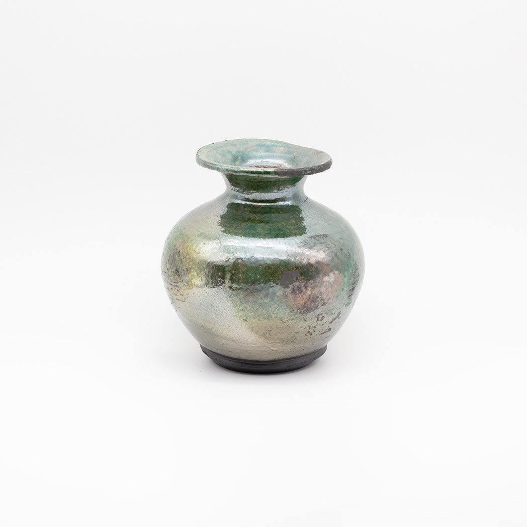 A small ceramic bud vase with a rounded body, flared rim, and dark base, featuring a textured metallic green and silver glaze.