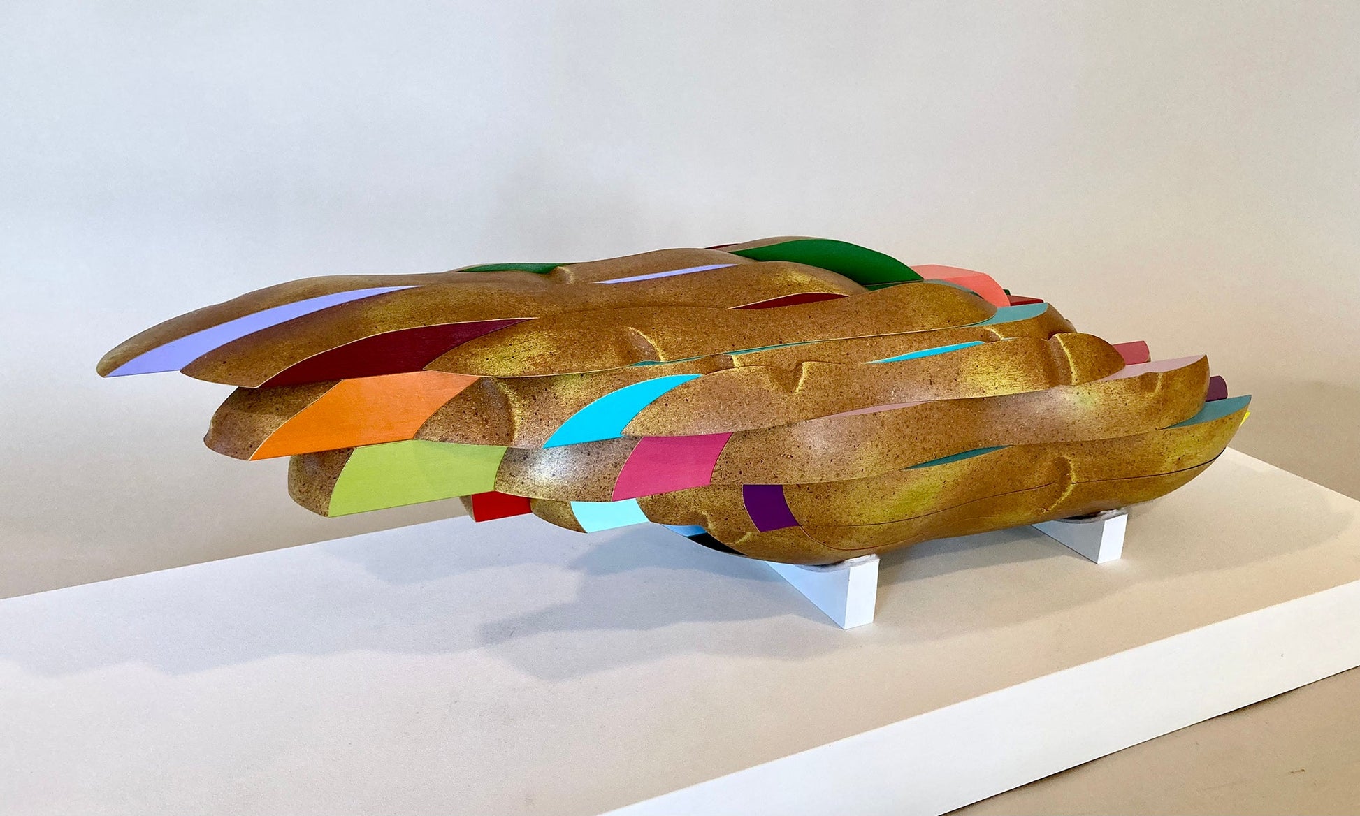 Wooden sculpture of a potato cut into fry shapes. Where all of the shapes are separate from the potato there are different colors orange, red, purple, blue, and pink.2019 6.5"x15"x7" painted wood Sean O'Meallie
