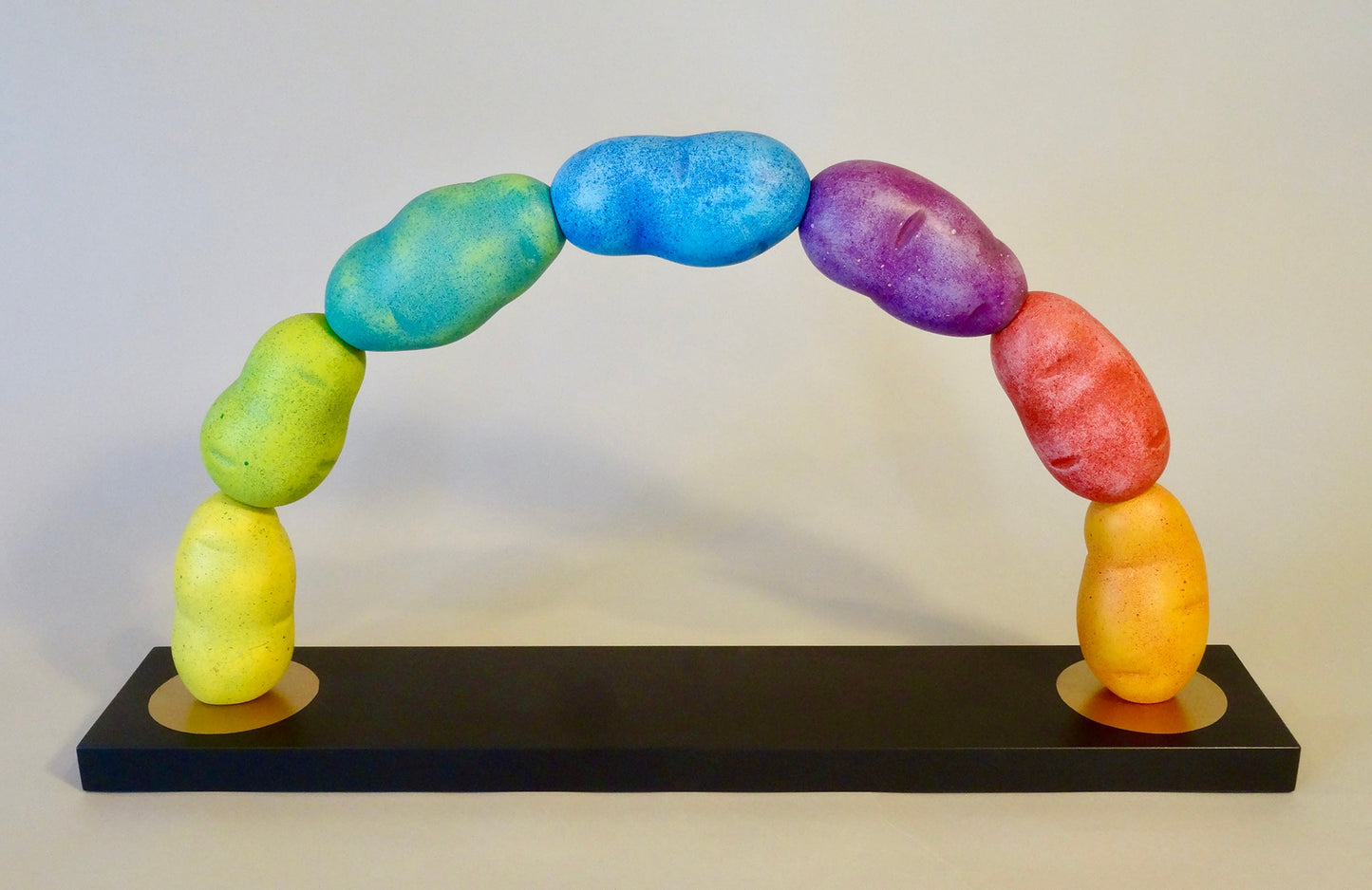Wooden sculpture of seven potatoes arranged and painted in a rainbow formation. 2019 13"x24"x4.5" painted wood by Sean O'Meallie